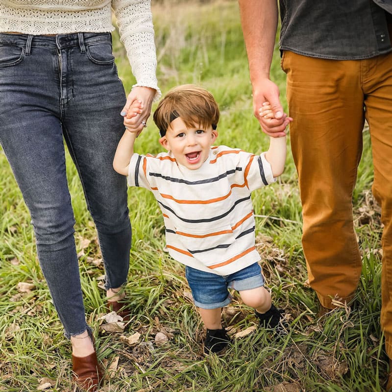 Otto holding his mom and dads hands while walking outside.